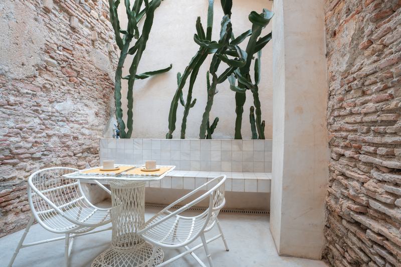 Patio interior con muros de piedra vista, cactus y mesa de forja blanca