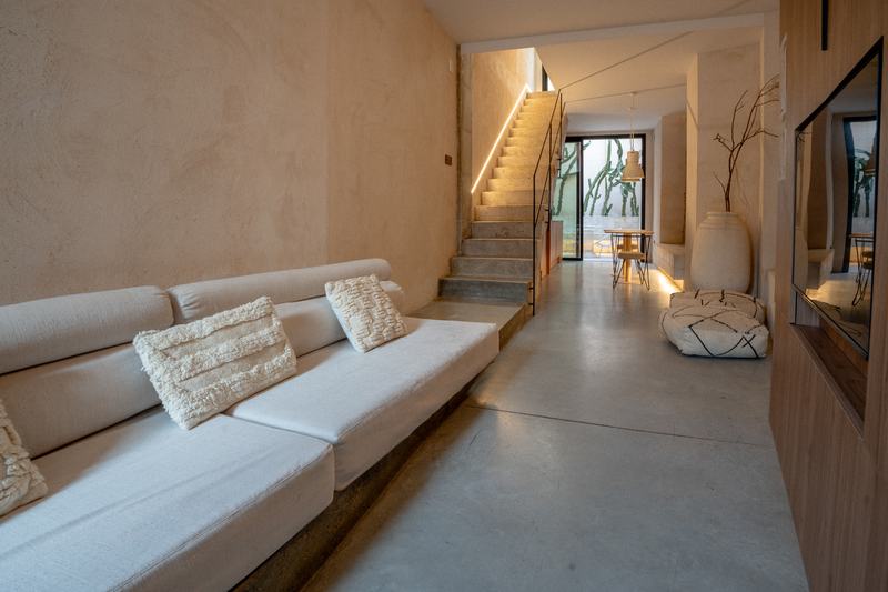 Salón alargado con sofá corrido, escalera iluminada y patio al fondo
