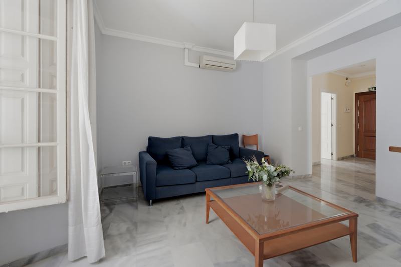 Salón con sofá azul junto al balcón y mesa baja de cristal