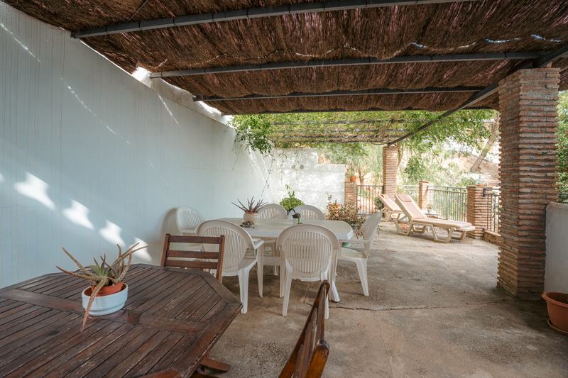 Terraza cubierta con mesa larga y muro encalado